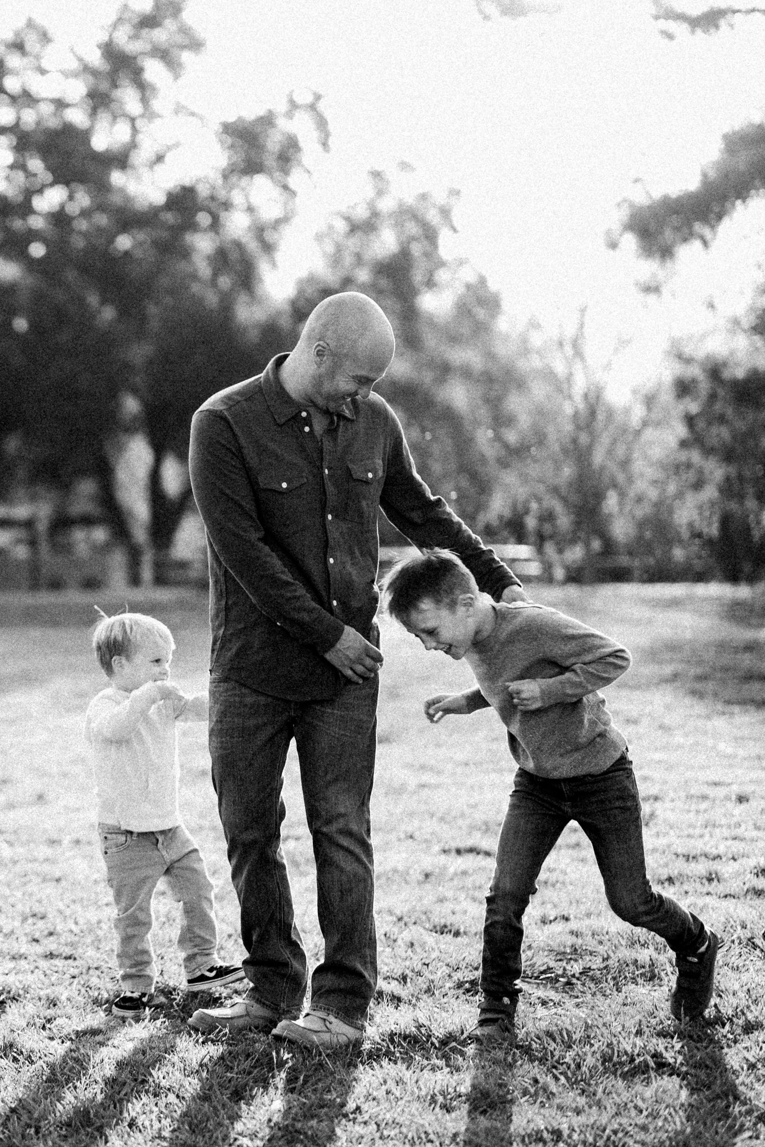 Black and white photo of playful moments between a father and children in a park.
