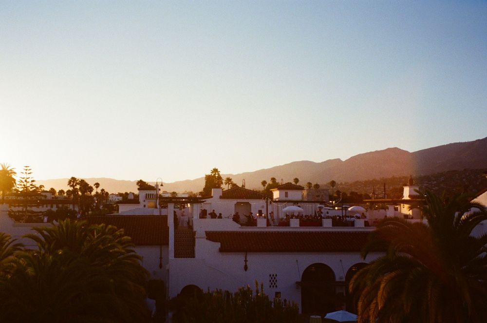 Panoramic view of desert mountains and white buildings at sunset with palm trees in silhouette.