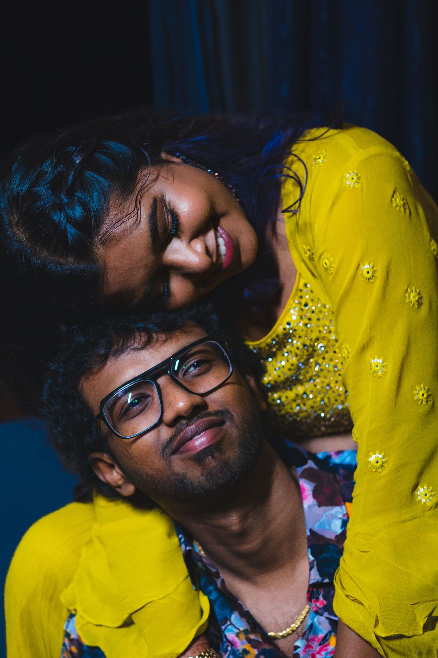 A playful couple in yellow and floral attire pose intimately for a portrait.