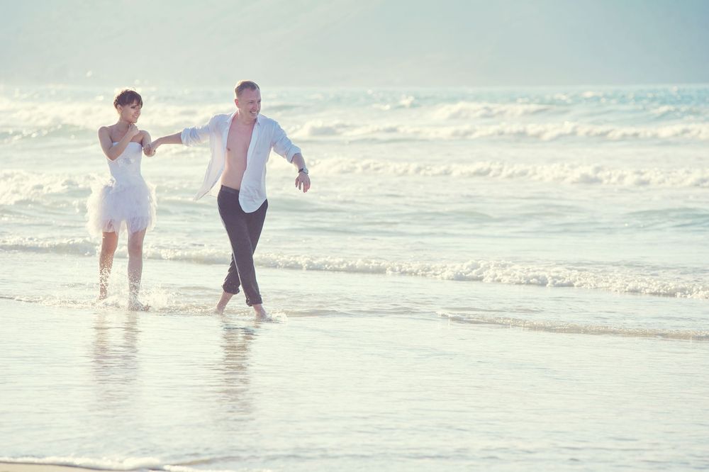 Joyful wedding couple walking on the beach, candid destination wedding photography