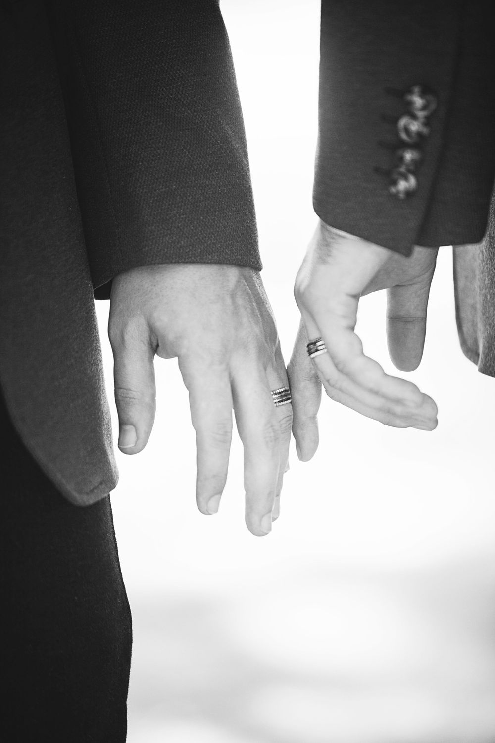 Black and white same-sex wedding detail of two grooms holding hands, inclusive fine art wedding photography