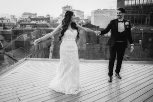A couple shares a romantic moment on a wooden deck overlooking a waterfront cityscape at sunset.