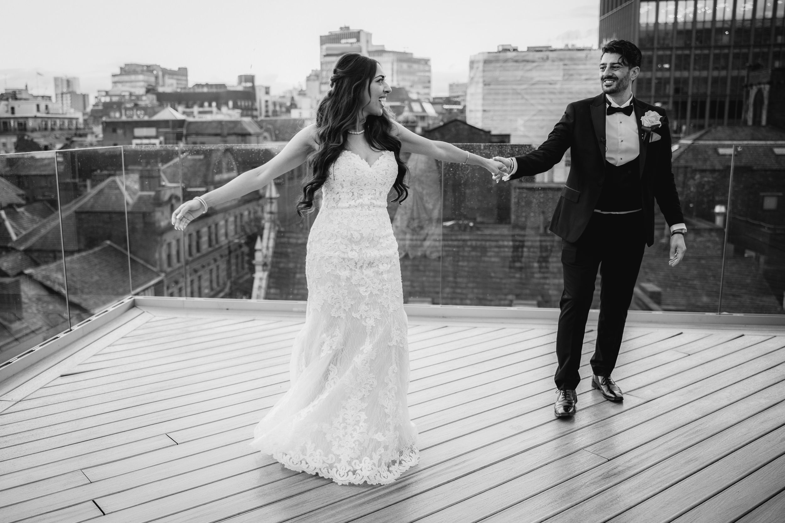A couple shares a romantic moment on a wooden deck overlooking a waterfront cityscape at sunset.