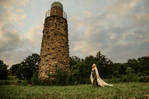 Stone tower ruins stand against a cloudy sunset sky in a grassy field.