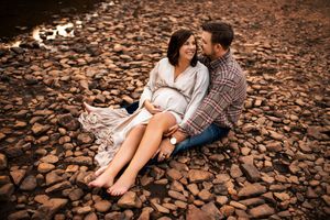 Couple sitting on autumn leaves covered ground during outdoor photoshoot with warm lighting.
