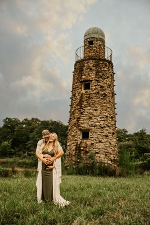Romantic photos near stone tower ruins at sunset in a grassy field.