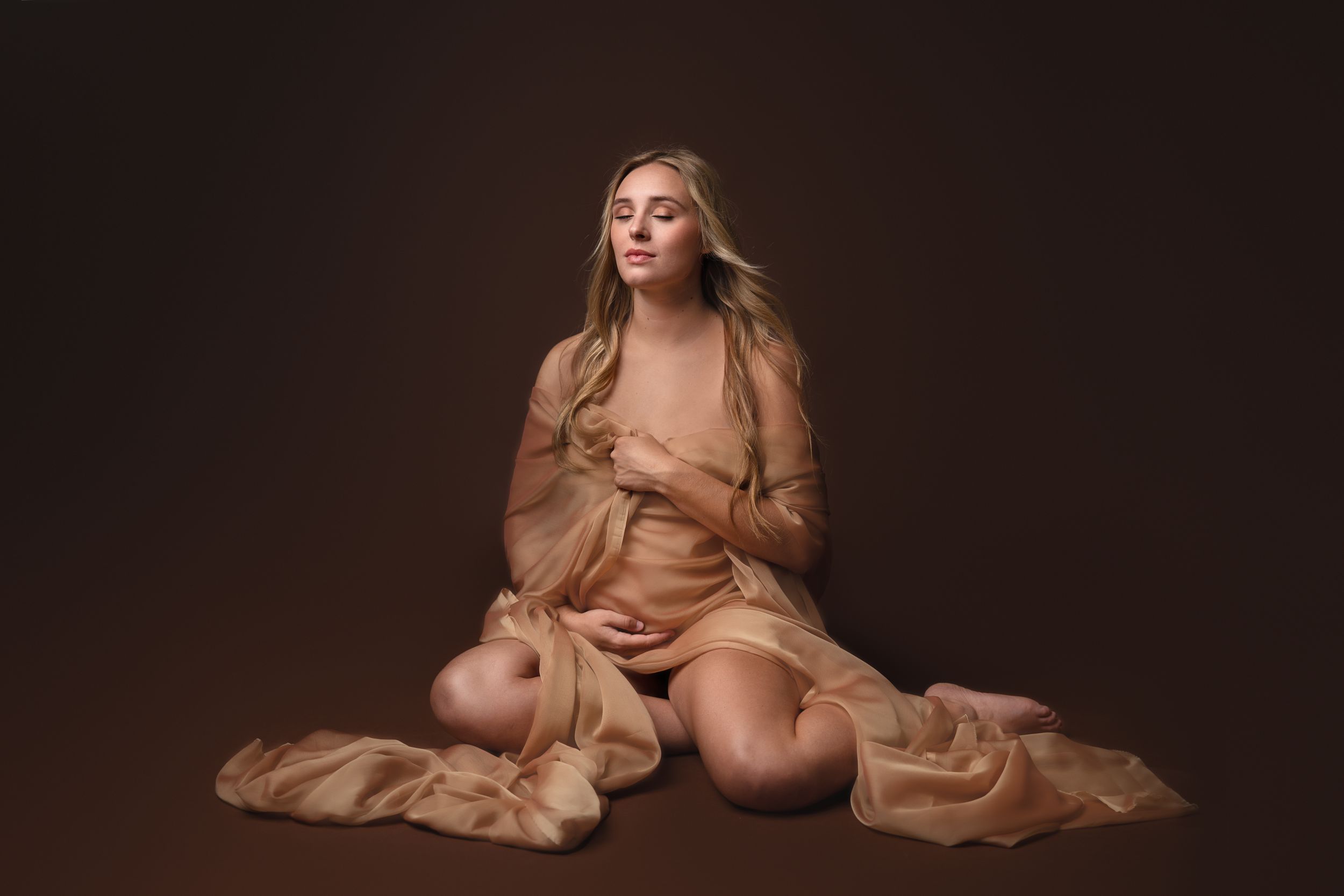 A dreamy portrait featuring someone wrapped in flowing beige fabric against a dark background.