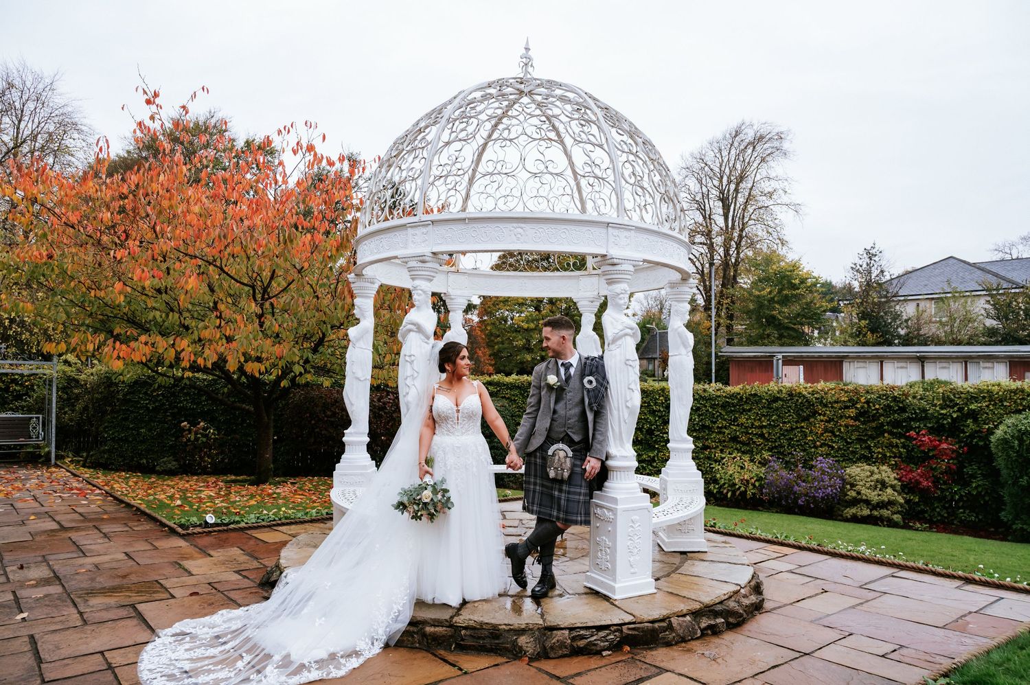 A romantic wedding couple poses on a wooden dock overlooking a serene lake with rolling hills in the background.