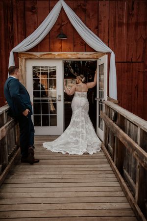 A rustic wedding scene at a barn entrance with a decorative white fabric draped over French doors and wooden boardwalk.
