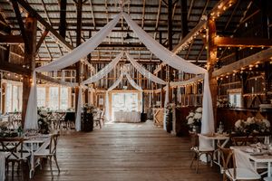 Rustic barn wedding venue interior decorated with white drapes and string lights for reception.