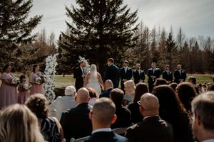 An outdoor wedding ceremony taking place on a lawn with evergreen trees in the background on an overcast day.