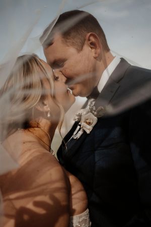 A romantic wedding portrait showing an intimate moment between newlyweds under a flowing veil.