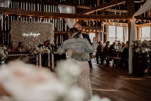 A couple shares their first dance in a rustic barn wedding venue with wooden beams and string lights overhead.