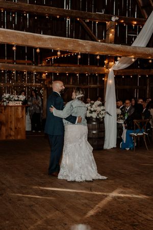 A couple shares their first dance in a rustic barn wedding venue decorated with string lights and white draping.