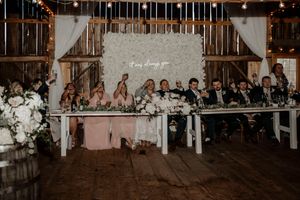 A long head table at a rustic barn wedding reception with string lights illuminating the wooden interior and decor.