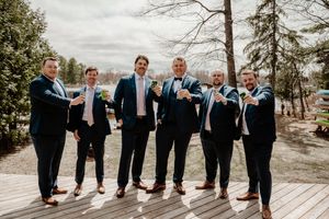 Groomsmen wearing matching suits and blue ties stand together on a wooden deck surrounded by trees.