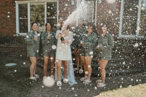 A group celebrates outdoors with champagne spraying and confetti while posing together in casual attire.