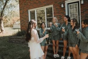 A group in matching gray robes stands together on a lawn in front of a brick house during a celebratory moment.