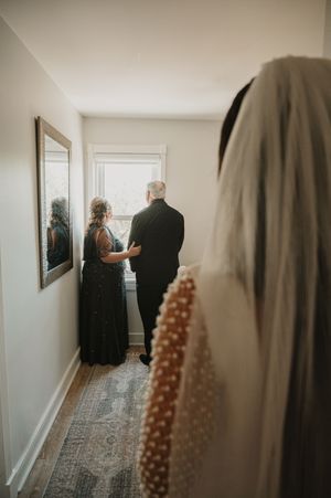 A wedding dress with pearl details hangs in a hallway with a vintage style runner.
