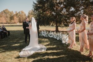 An outdoor wedding ceremony takes place on a sunny autumn day with bridesmaids in blush dresses watching the couple.
