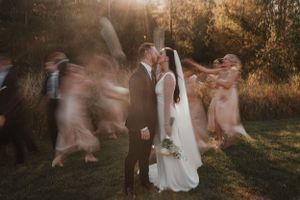 A couple shares an intimate moment at sunset while motion-blurred figures dance around them in a golden field.