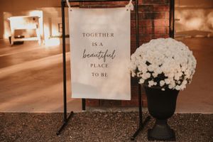 A wedding sign reading 'Together is a beautiful place to be' displayed next to white floral arrangements.