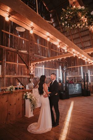 Romantic rustic barn wedding venue with string lights illuminating a couple on the wooden dance floor at sunset.