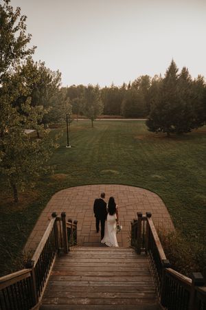 Couple standing on a romantic wooden footbridge surrounded by autumn trees and grass at sunset.