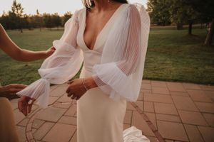 Modern bride in fitted white dress with dramatic sheer puff sleeves standing on outdoor patio at sunset.