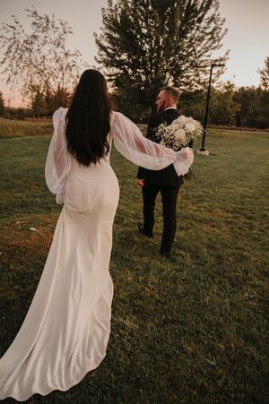 A romantic wedding photo on a grassy field at sunset with flowing white dress and bouquet details.