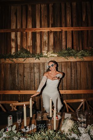 A figure poses at a rustic barn wedding reception with sunglasses, decorated with candles and floral arrangements.