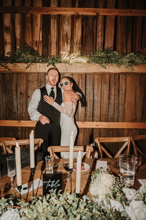 A rustic barn wedding reception with a wooden backdrop, decorative greenery, and table settings with white floral centerpieces.