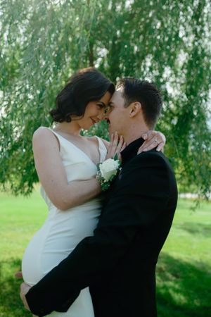 Romantic newlyweds embrace under a weeping willow tree during wedding photoshoot.