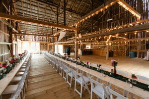 Rustic wooden barn interior decorated with string lights and white chairs set up for an elegant wedding reception.