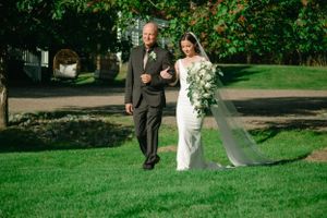 A traditional wedding processional on a lush green lawn with cascading white bouquet.