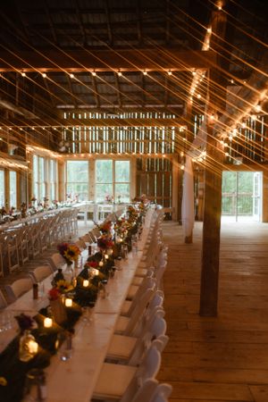 Long rustic barn reception tables decorated with candlelight and string lights creating warm ambiance for wedding dinner.