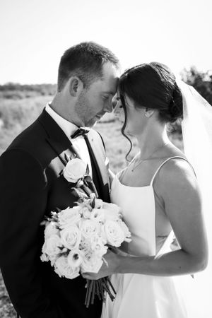 A romantic black and white wedding photo showing a tender moment with the couple holding a bouquet of white roses.