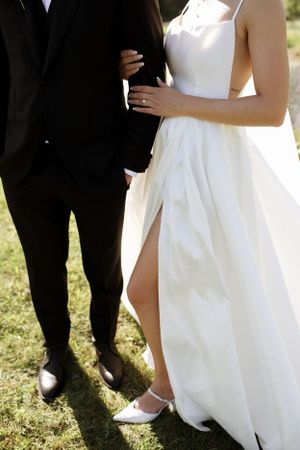 Close-up shot of formal wedding attire showing a white dress with side slit and black tuxedo.