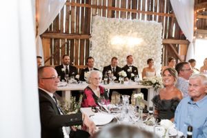 Wedding reception guests enjoying dinner and conversation inside a rustic barn venue with wooden beams.