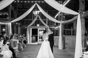 A couple shares their first dance under draped fabric and string lights in a rustic barn wedding venue.