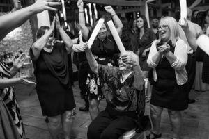 Black and white photo of wedding guests dancing with raised arms on dance floor at reception.