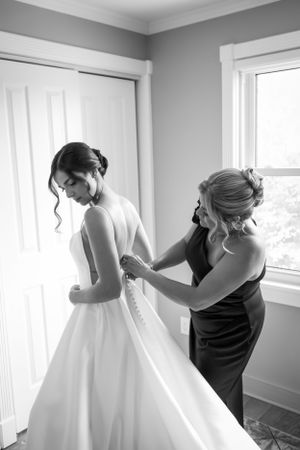 A tender moment during wedding preparations as final dress adjustments are made in a sunlit room.