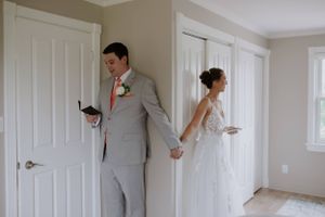Bride and groom hold hands while standing on opposite sides of a door before their wedding ceremony.