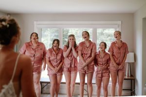 A group in matching pink satin pajama sets reacting with excitement during wedding preparations.
