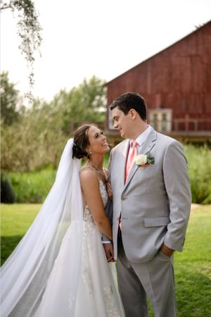 A wedding couple shares an intimate moment on a lawn in front of a rustic red barn on their special day.