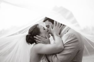 Black and white romantic wedding photo showing a tender kiss between newlyweds under a flowing veil.
