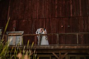 Couple shares romantic moment on wooden balcony of vintage red barn at sunset.