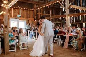 A couple shares an intimate moment on their wedding day inside a rustic barn reception decorated with string lights.