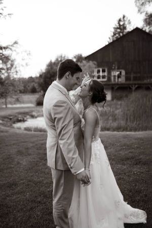 A romantic black and white outdoor wedding photo of a couple sharing an intimate moment by a rustic barn.