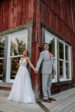 A playful wedding photo featuring a couple posing back-to-back against a red barn with white-framed windows.